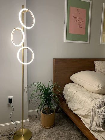 A tall gold floor lamp featuring three branches, each supporting a glowing ring.