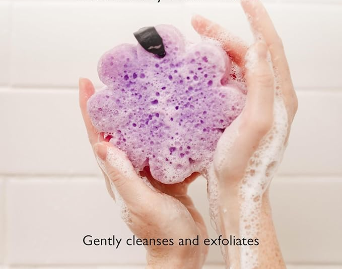 A pair of hands holding a flower-shaped body wash buffer, infused with lavender scent. The accompanying text reads: