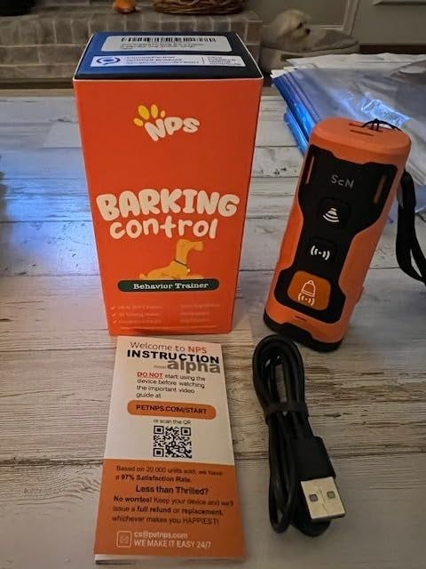 A barking control device, complete with packaging, instruction manual, and a USB charger on a table.