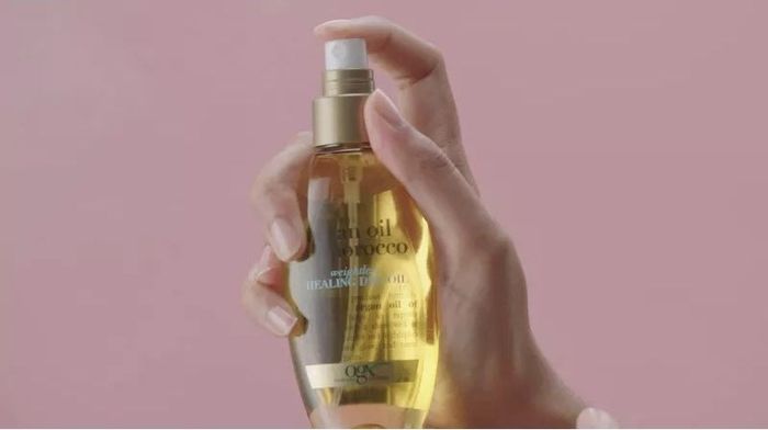 A hand holding a bottle of OGX Extra Strength Coconut Miracle Oil, Healing Dry Oil for hair