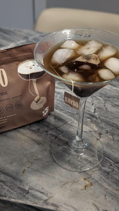A martini glass filled with iced coffee martini, placed next to a Sayso cocktail sachet on a marble surface.