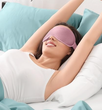 A model resting in bed, wearing a pink sleep mask