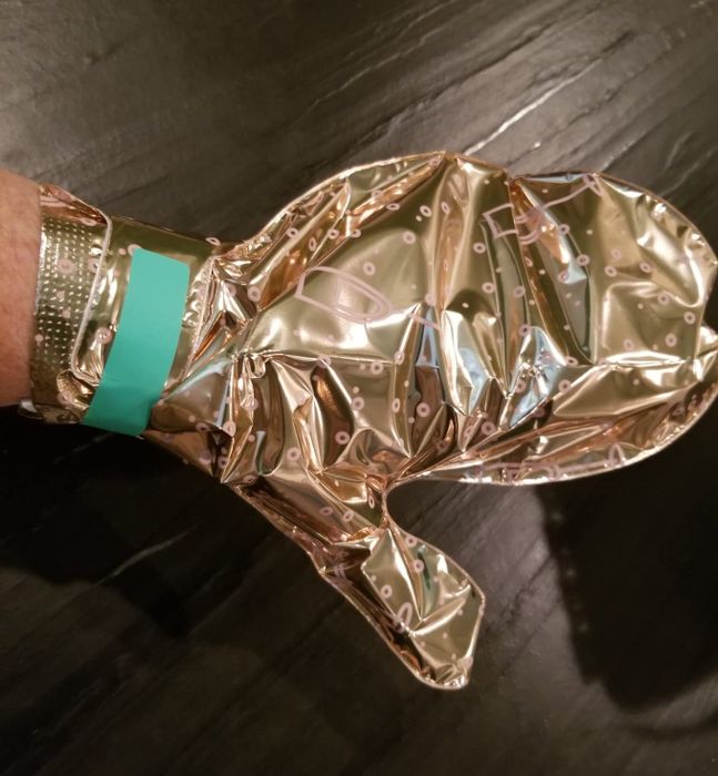 A shiny, metallic oven mitt with a perforated design, showcased with a hand model. It was featured in a shopping article on kitchen accessories.