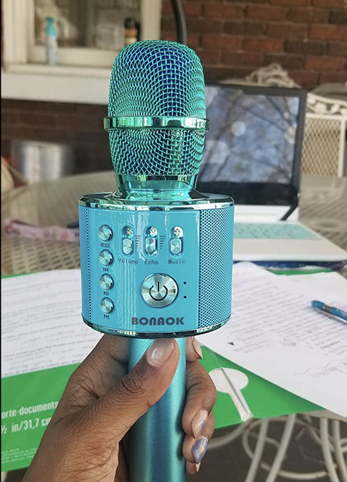 A reviewer holding a blue karaoke microphone with buttons.