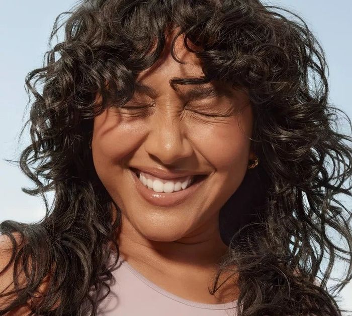 Smiling model with curly hair and closed eyes, with text stating 