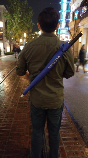 The reviewer casually carrying the closed umbrella on their shoulder.