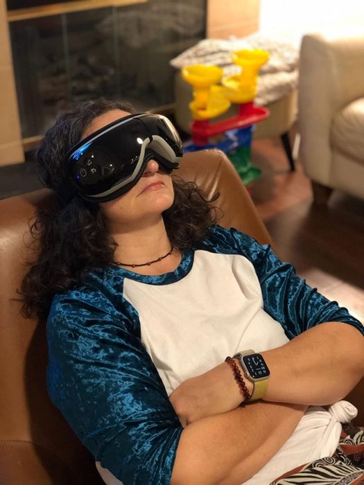 A reviewer wearing a white eye massager with gray cushioning at the nose, securely fastened around their head