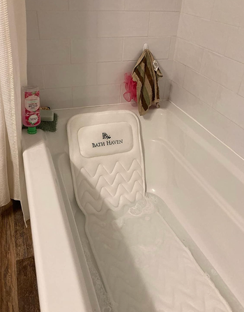 A white mat placed over a bathtub, with a pillow propped up on it