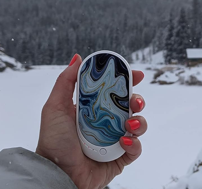 A reviewer holding the hand warmer in the ocean wave color while out in the snow.