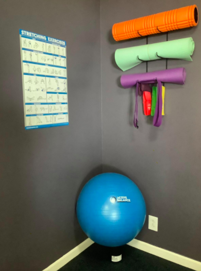 The reviewer stores red, green, and yellow yoga mats, along with resistance bands, neatly on their home gym wall mount.