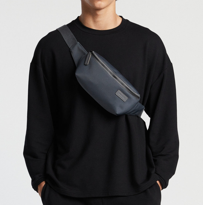 A model wears a blue leather fanny pack across their torso, showcasing its stylish and functional design.