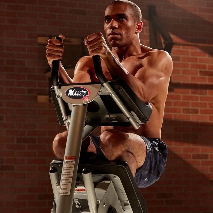 A shirtless model uses the ab coaster to engage their core.