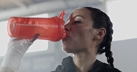 A model drinks from an orange BlenderBottle, ready for hydration.