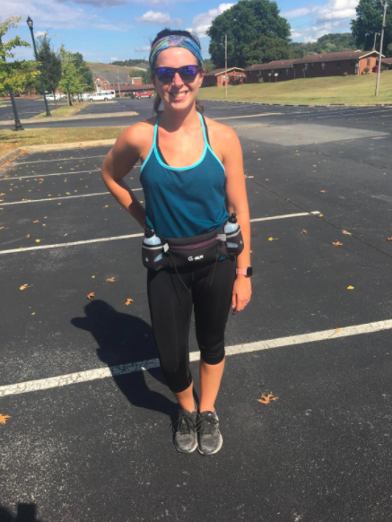 Reviewer sports a black and purple hydration belt, paired with black capri leggings, a blue tank top, and gray sneakers for a complete look.
