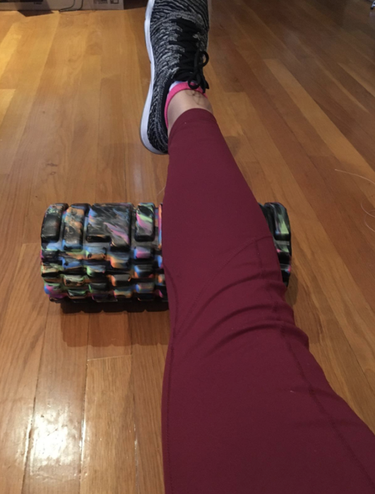 A reviewer in red leggings uses the same style of foam roller to massage their calf muscles, aiding in muscle recovery.