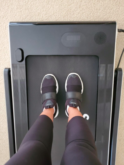 Reviewer steps onto a black treadmill with the riser lowered for a compact setup.