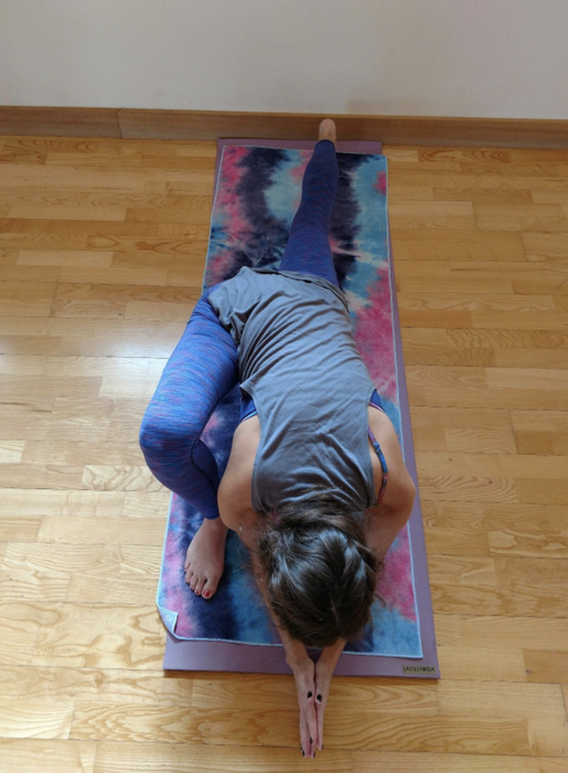 The reviewer strikes a yoga pose on a vibrant pink and purple tie-dye towel, showcasing its bold and comfortable design.