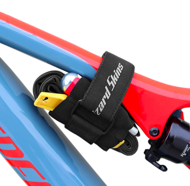 A black bike utility strap holds tools and gear firmly on a blue and red bike frame.