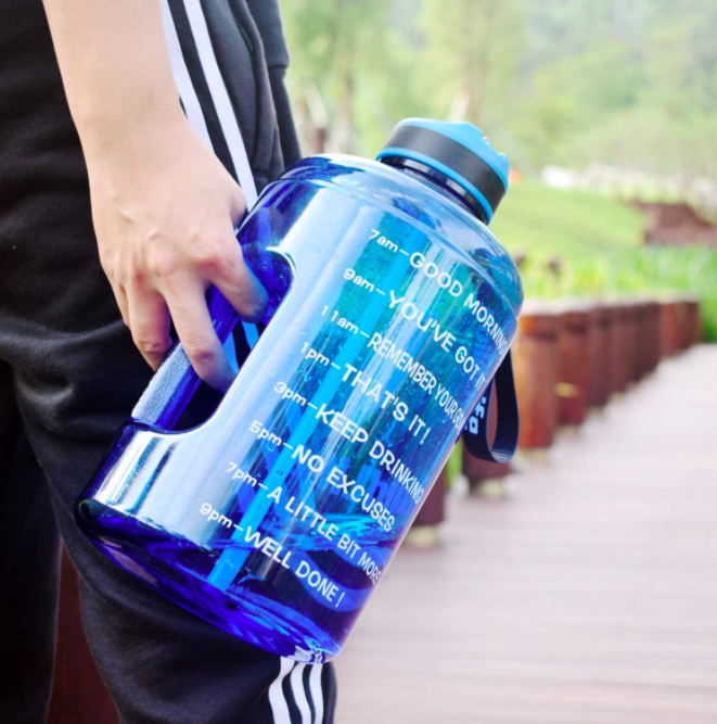 Hand holds a blue water bottle with motivational time markers and encouraging words printed on the side to keep them motivated throughout their workout.