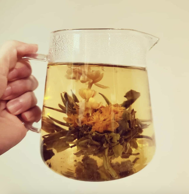 The reviewer holding a clear pitcher filled with blooming tea.