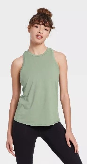 The model is wearing a sage green racerback tank top paired with black leggings.
