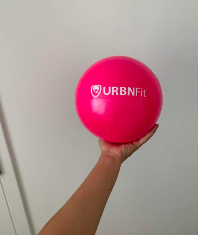 Reviewer holds a mini pink Pilates ball in front of a white wall, gripping it with one hand.