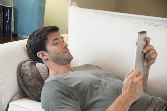 person relaxing with a neck massage pillow while looking at an iPad
