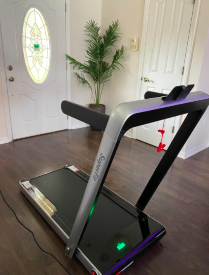 Reviewer demonstrates the same black treadmill with the riser raised, set up in a compact space near their front entrance.