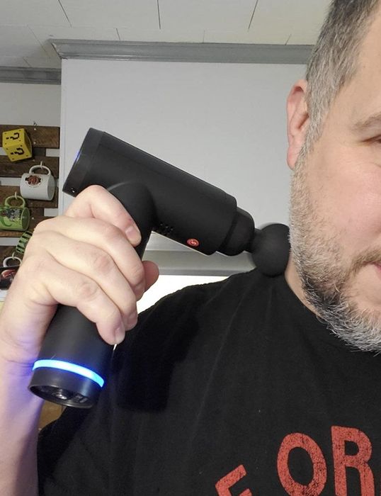 A person uses a massage gun to target their shoulder, relieving muscle tension.