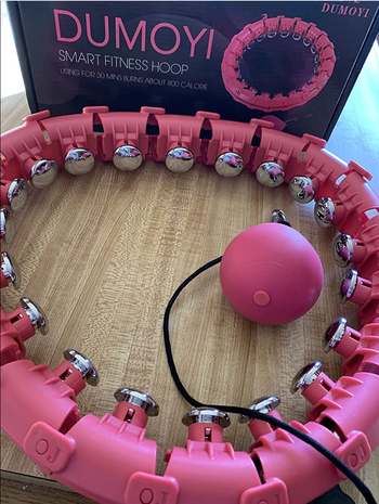 A pink version of the weighted hoop rests on the floor, ready for its next session.
