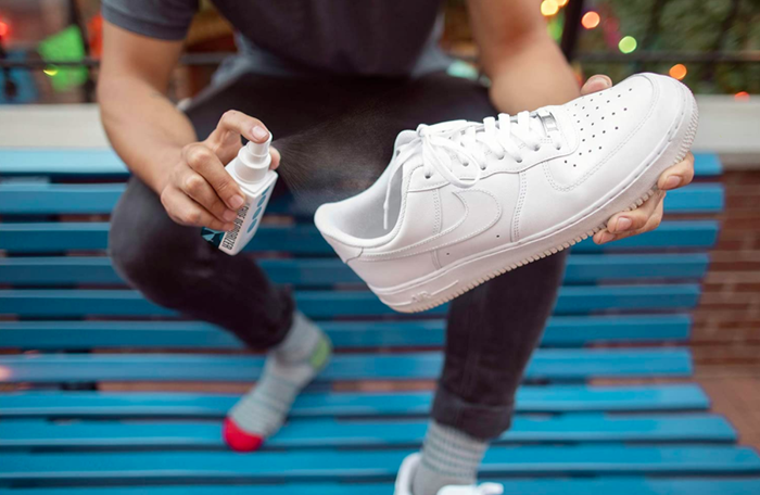 Model sprays shoe deodorizer into a pair of white Nike basketball shoes.