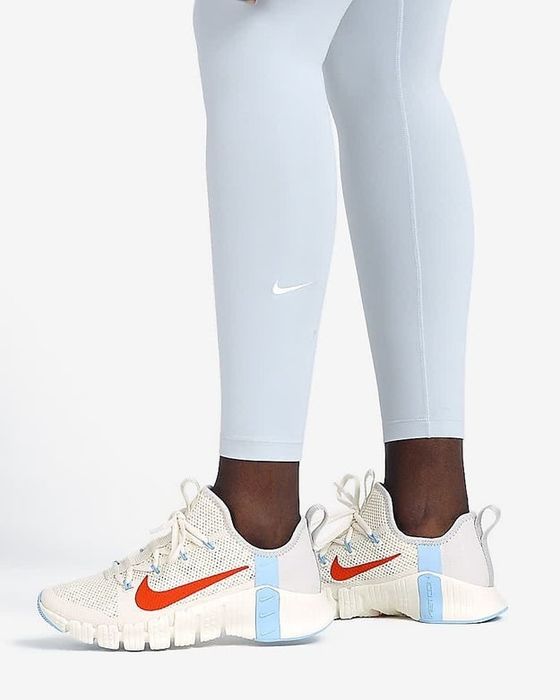 A model shows off white training shoes with blue and orange accents on the sides