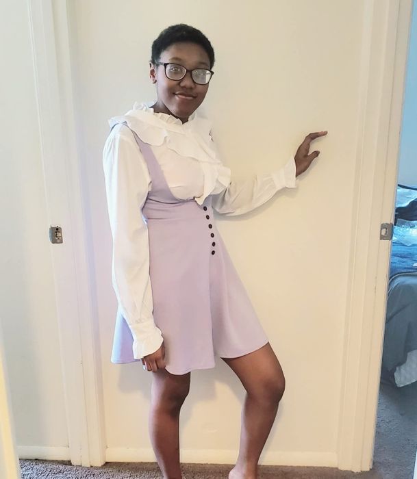 A reviewer wearing a lavender pinafore dress with suspenders.