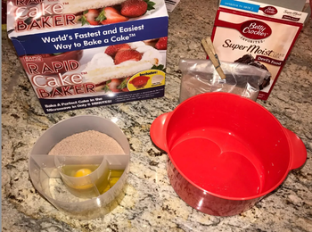 A red cake maker bowl next to a clear bowl containing cake mix, oil, and an egg