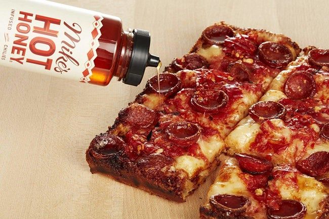 A bottle of honey drizzling over a slice of pepperoni pizza.