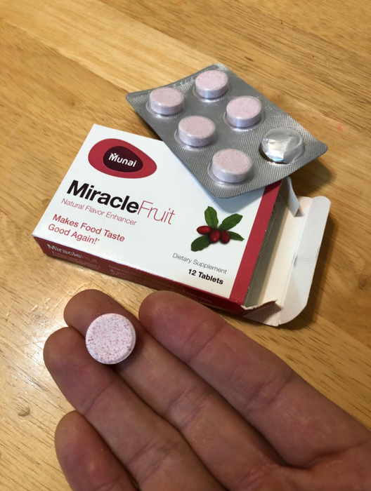 A reviewer holding a pink tablet next to a box of Miracle Berries