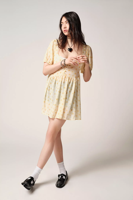 A model wearing a yellow babydoll dress adorned with floral patterns.