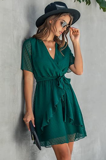 A model wearing a forest green dress with short sleeves and a ruffle detail at the waist.