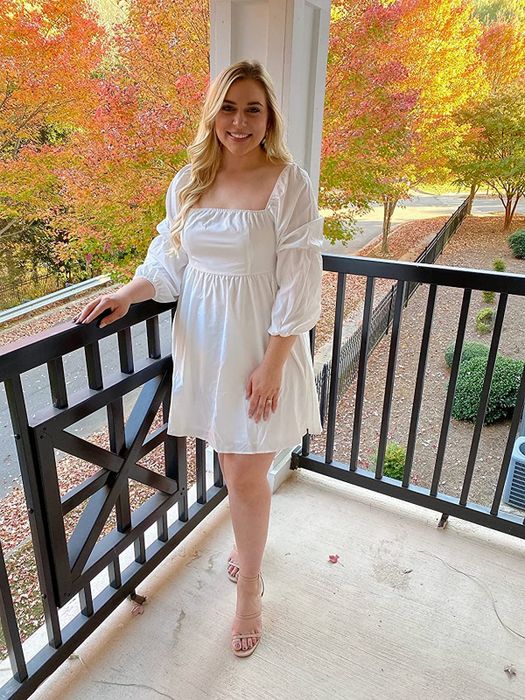 A reviewer in a white dress with a square neckline and balloon sleeves.
