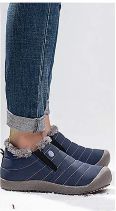 A model wearing ankle-high boots with grey rubber soles, blue material with stitched accents, and faux fur lining the top of the boots