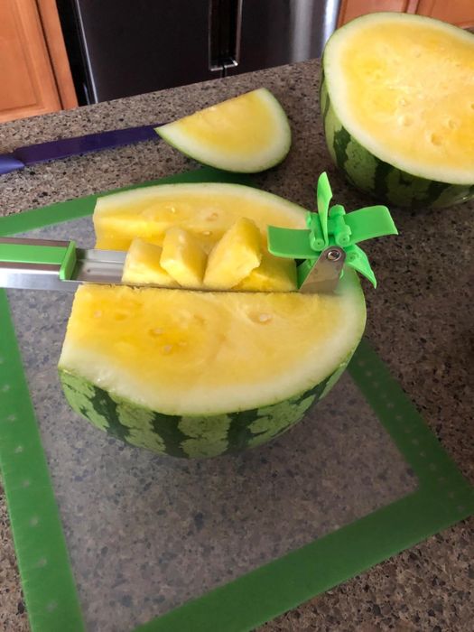 A reviewer's photo of the stainless steel cutter in use on a yellow watermelon
