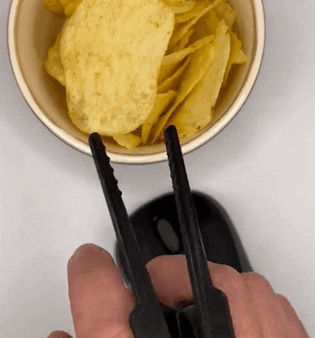 A model wearing a small chopstick-like device between two fingers, picking up a chip from a bowl with it