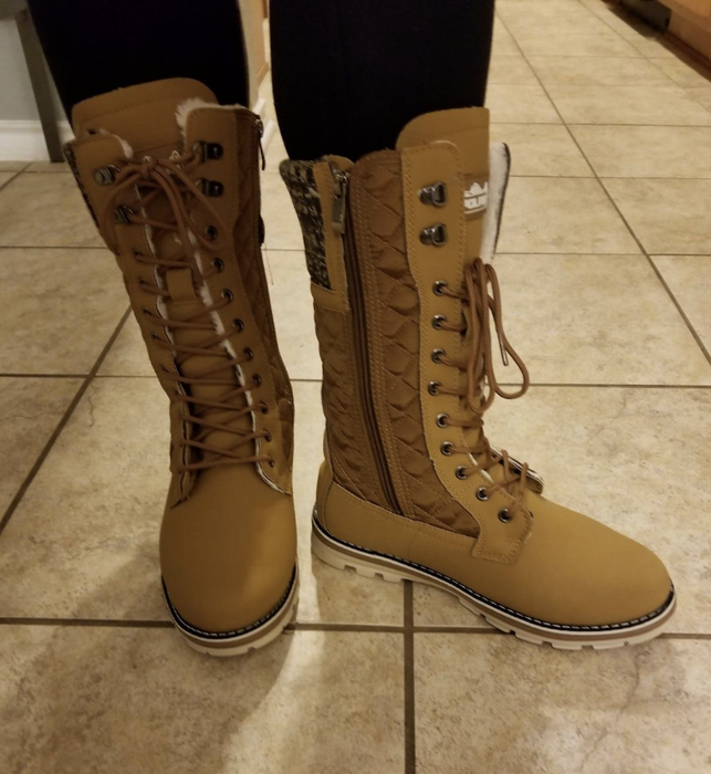A reviewer showcases the mid-thigh length lace-up boots in brown, featuring a zipper along the inner side.