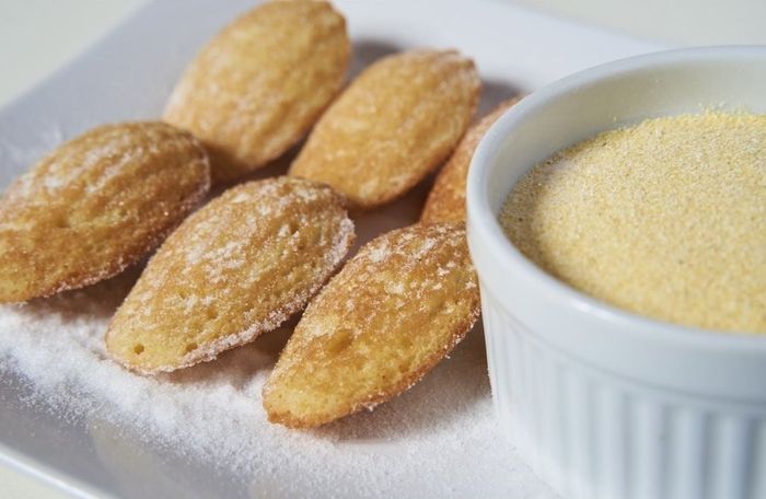 A plate of cornbread madeleines next to a bowl of cornmeal