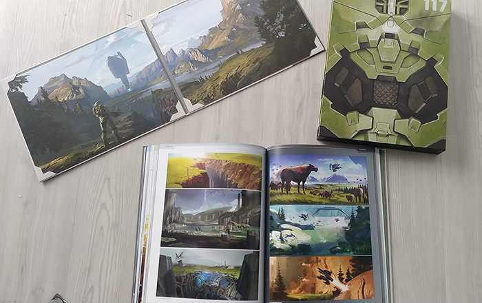 A reviewer's photos showcasing the deluxe edition art book of Halo Infinite, featuring high-quality artwork from the game.