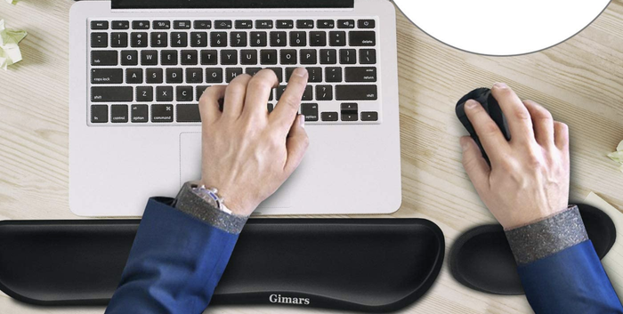 A model typing with one hand while using a mouse with the other, their wrists comfortably supported by ergonomic pads.