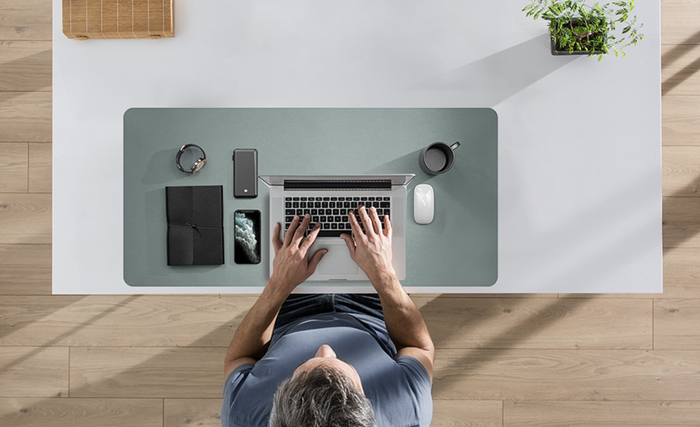 A person typing at their desk with the desk pad neatly positioned underneath their laptop and other items.
