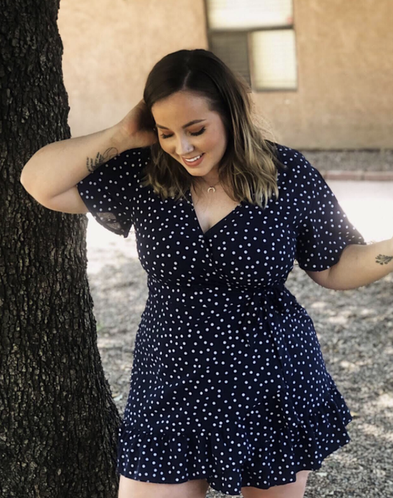 A reviewer wearing a short-sleeve V-neck dress with a polka dot print and a ruffled hem.