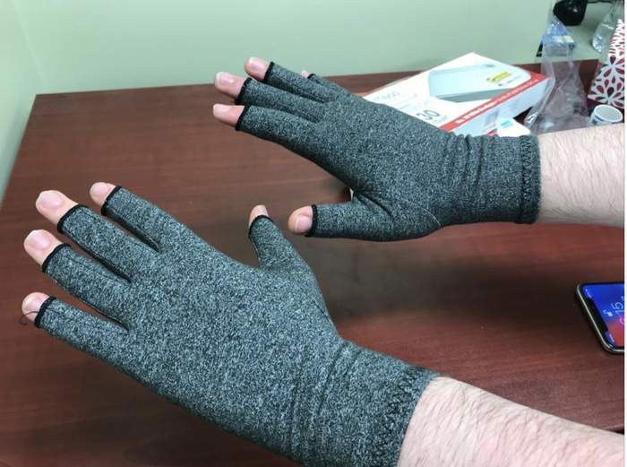 A reviewer wearing gray fingerless compression gloves on both hands.