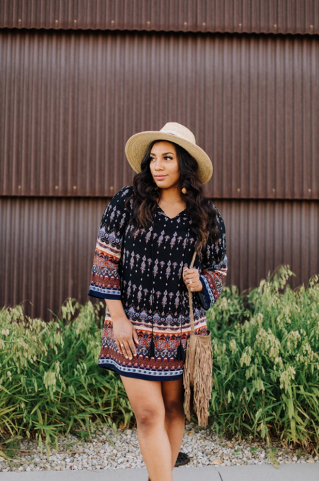 A reviewer wearing a long-sleeve midi dress in a boho-style print, accessorized with a bag and hat.